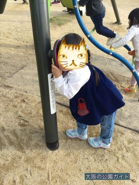 彩都西公園のバッタ遊具の音声電話を聞いている子供